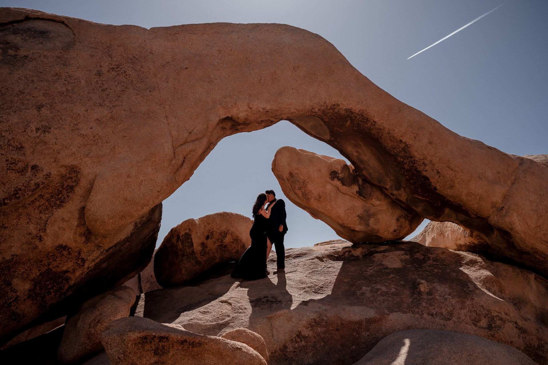 Couple kissing silhouetted under a desert rock arch in Joshua Tree