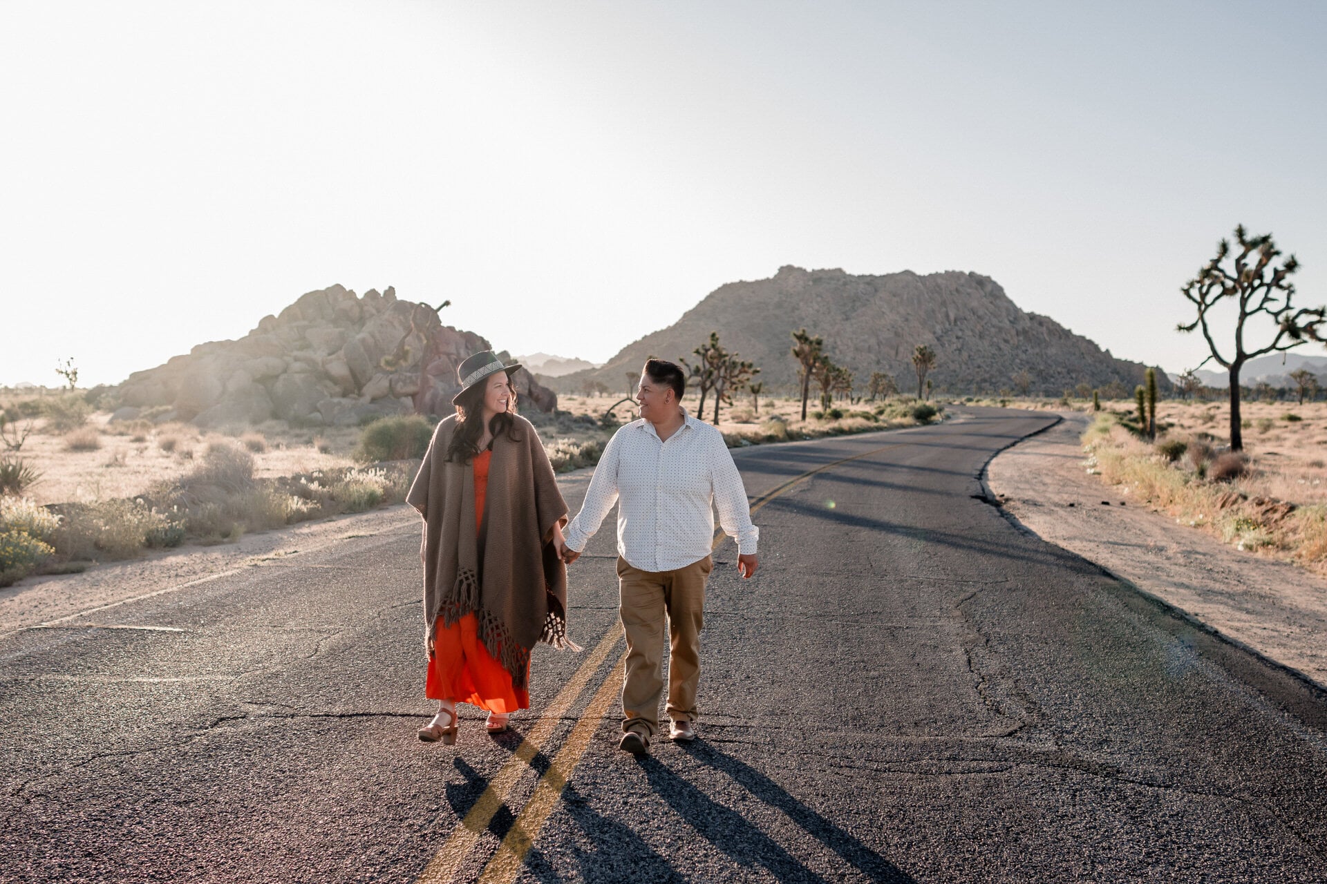Couple walking a desert road at golden hour among Joshua trees