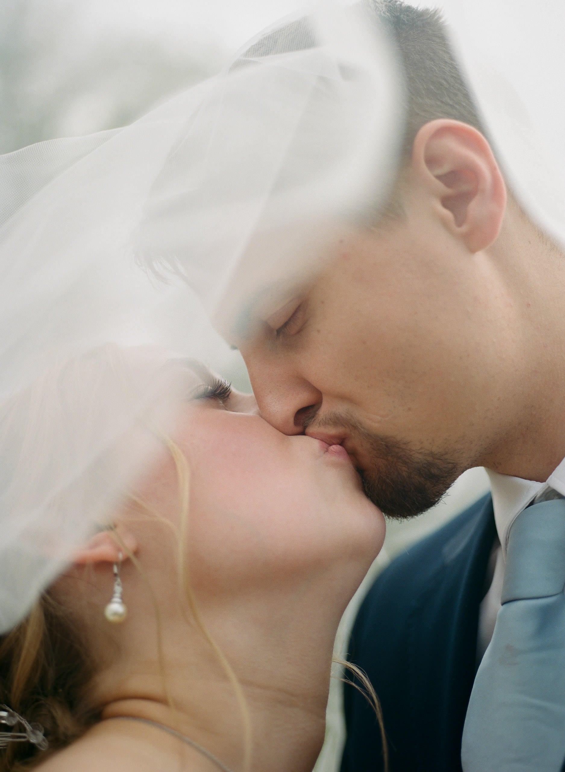 Close up film photograph of a bride and groom kissing beneath a soft veil
