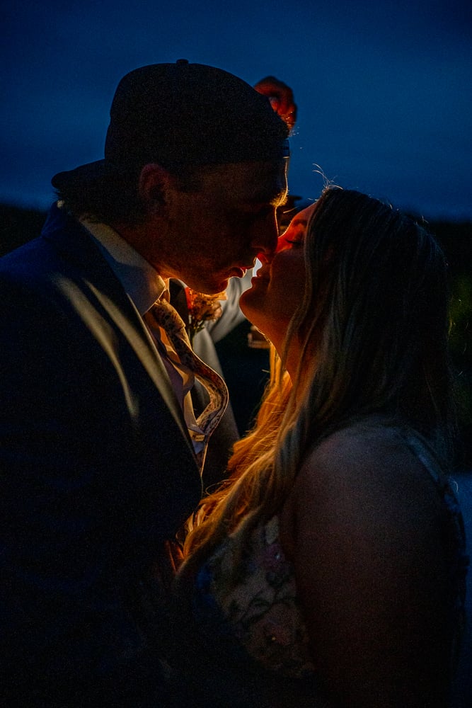 Couple sharing a kiss lit by warm light against a deep blue hour sky