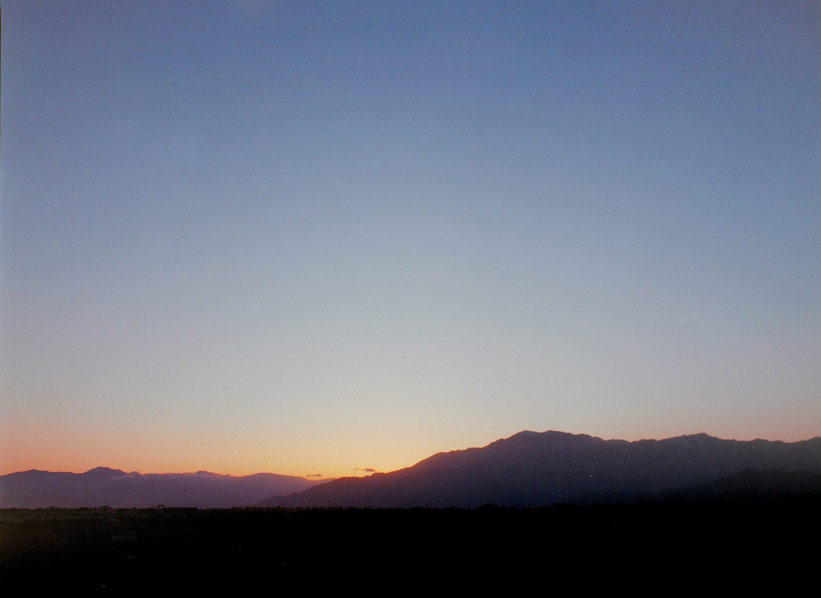 A soft dusk gradient of orange into blue over a dark mountain range silhouette.