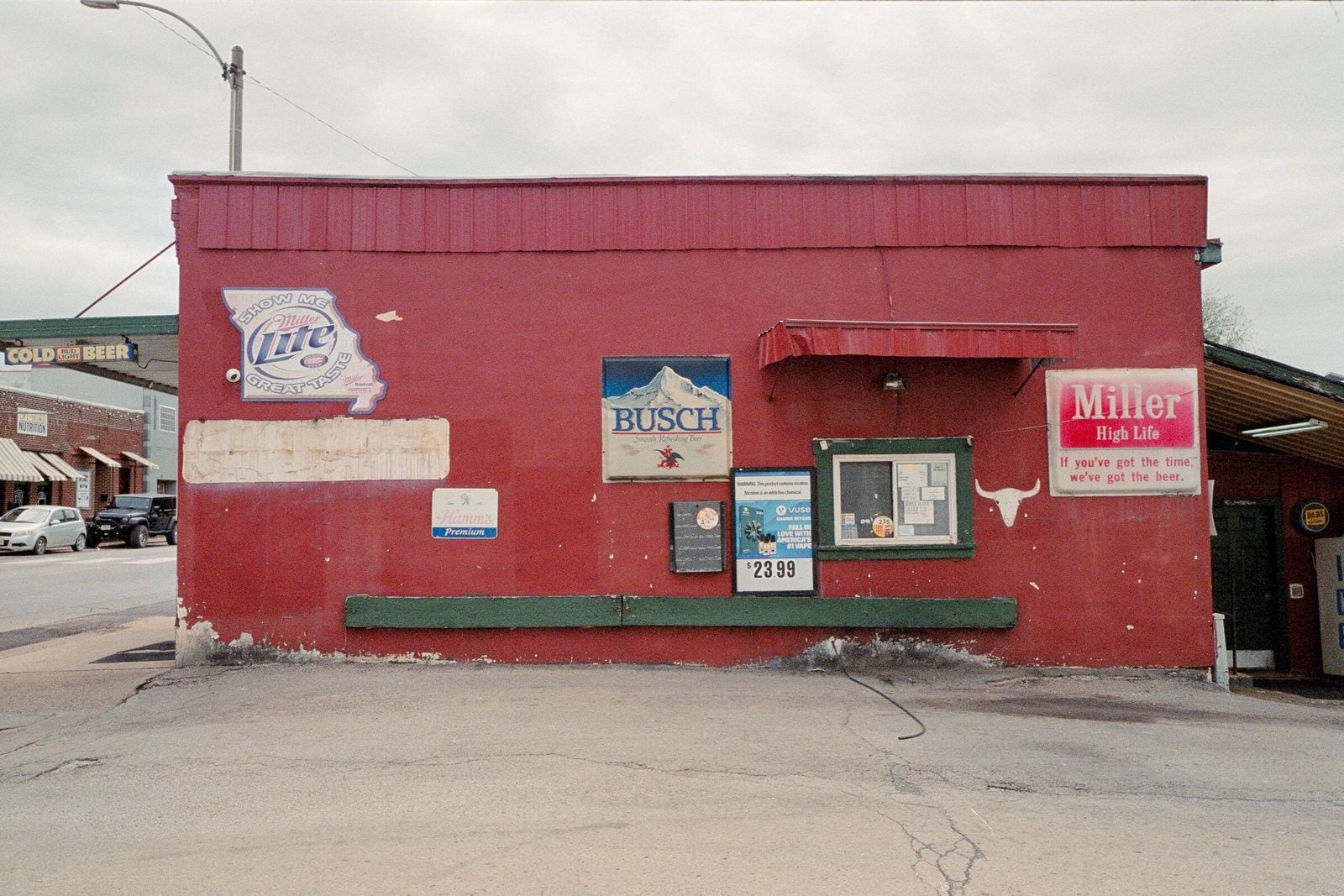 The red painted side wall of a small town tavern covered in vintage beer signs under an overcast sky.