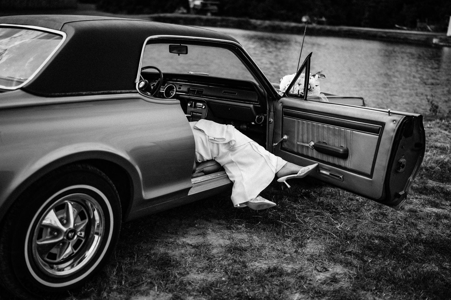 Black and white detail of a bride's leg and heel stepping out of a vintage convertible